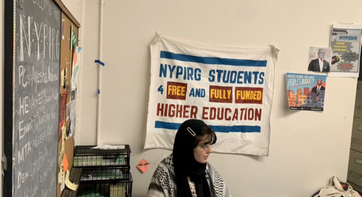 woman sits at desk with nypirg banner on wall