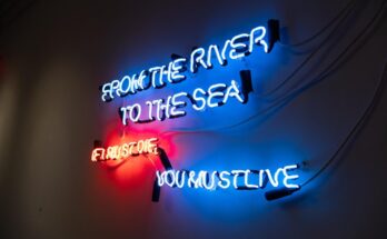 neon art piece reads "from the river to the sea"