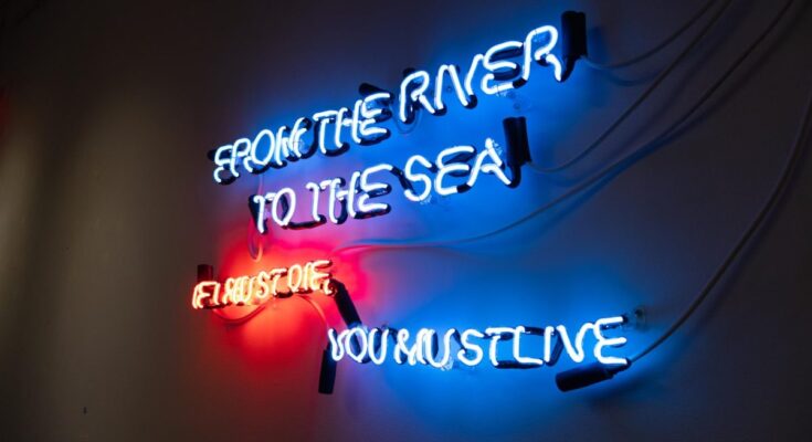 neon art piece reads "from the river to the sea"